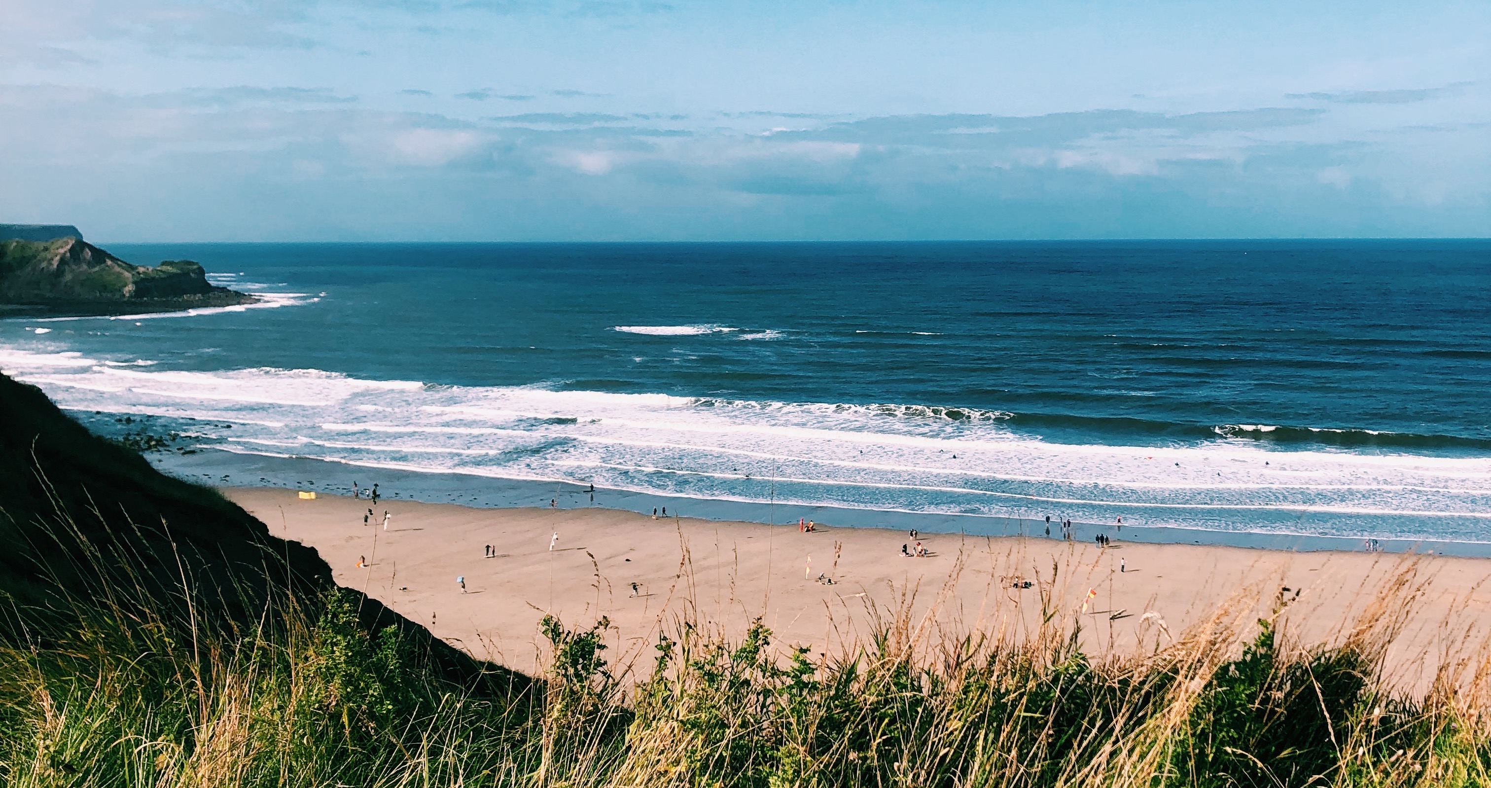 Shot from the cliffside, a teal blue sea crashes against golden sand